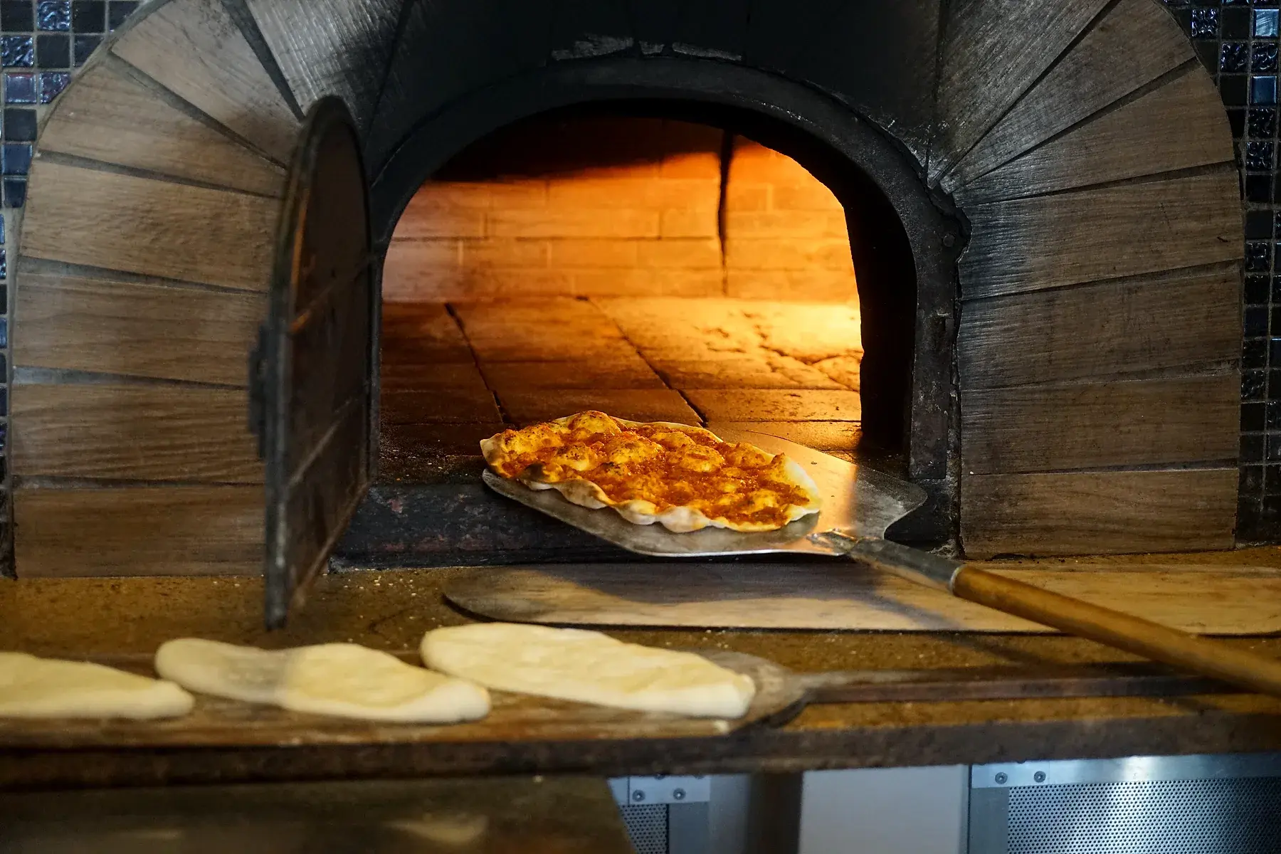 Pizza wird mit dem Schieber in den Steinofen gegeben