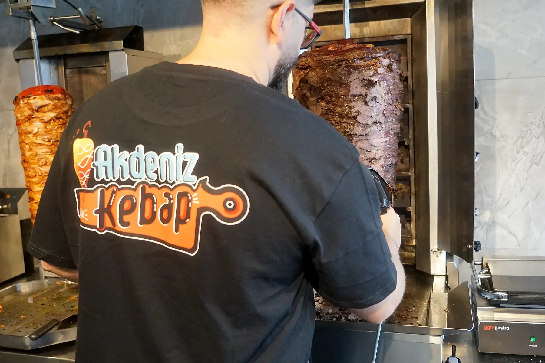 Mitarbeiter im Akdeniz-Kebap-Shirt am Döner Spieß