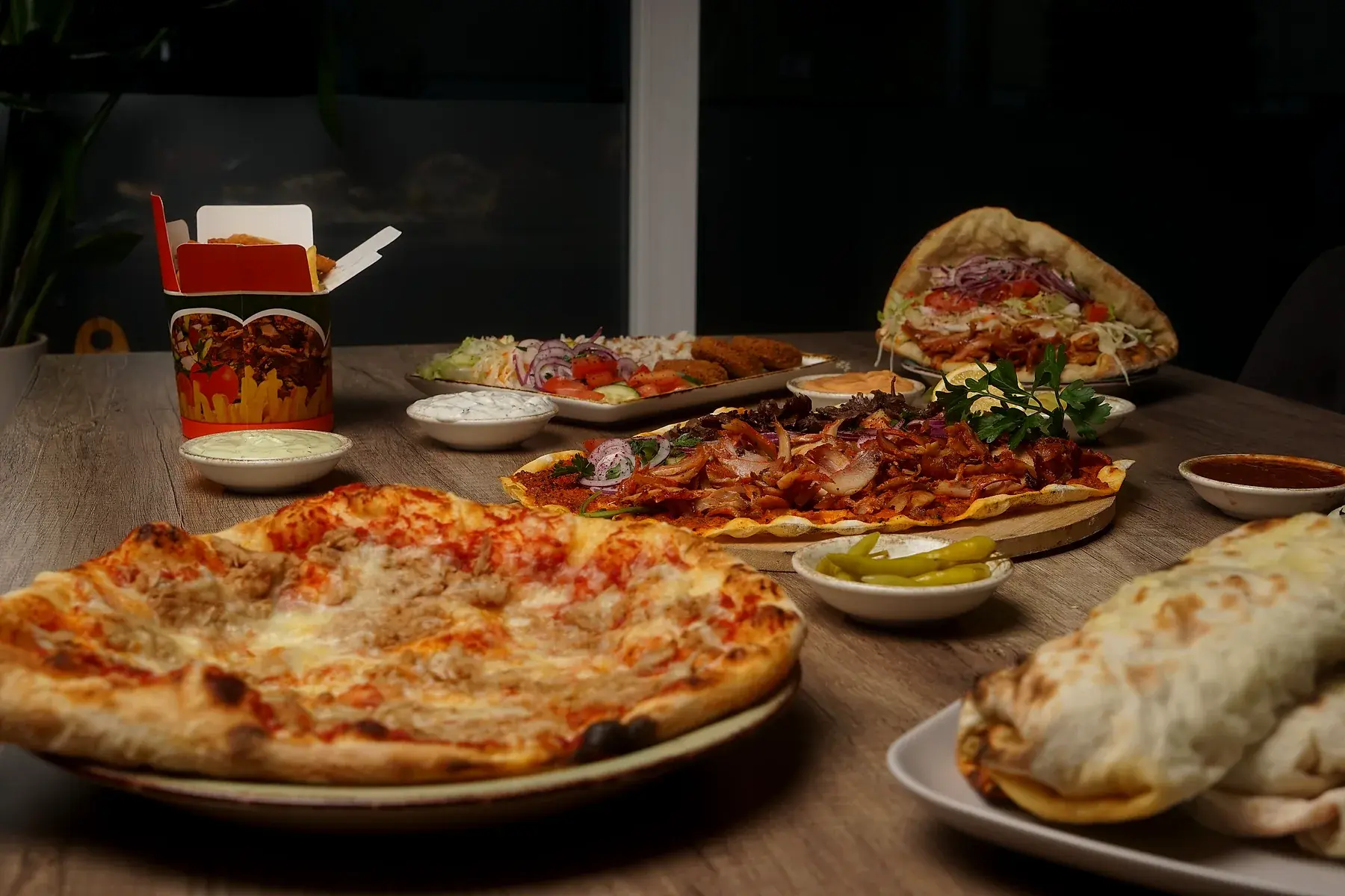 Gedeckter Tisch mit Pizza, Pide, Dürüm und Saucen